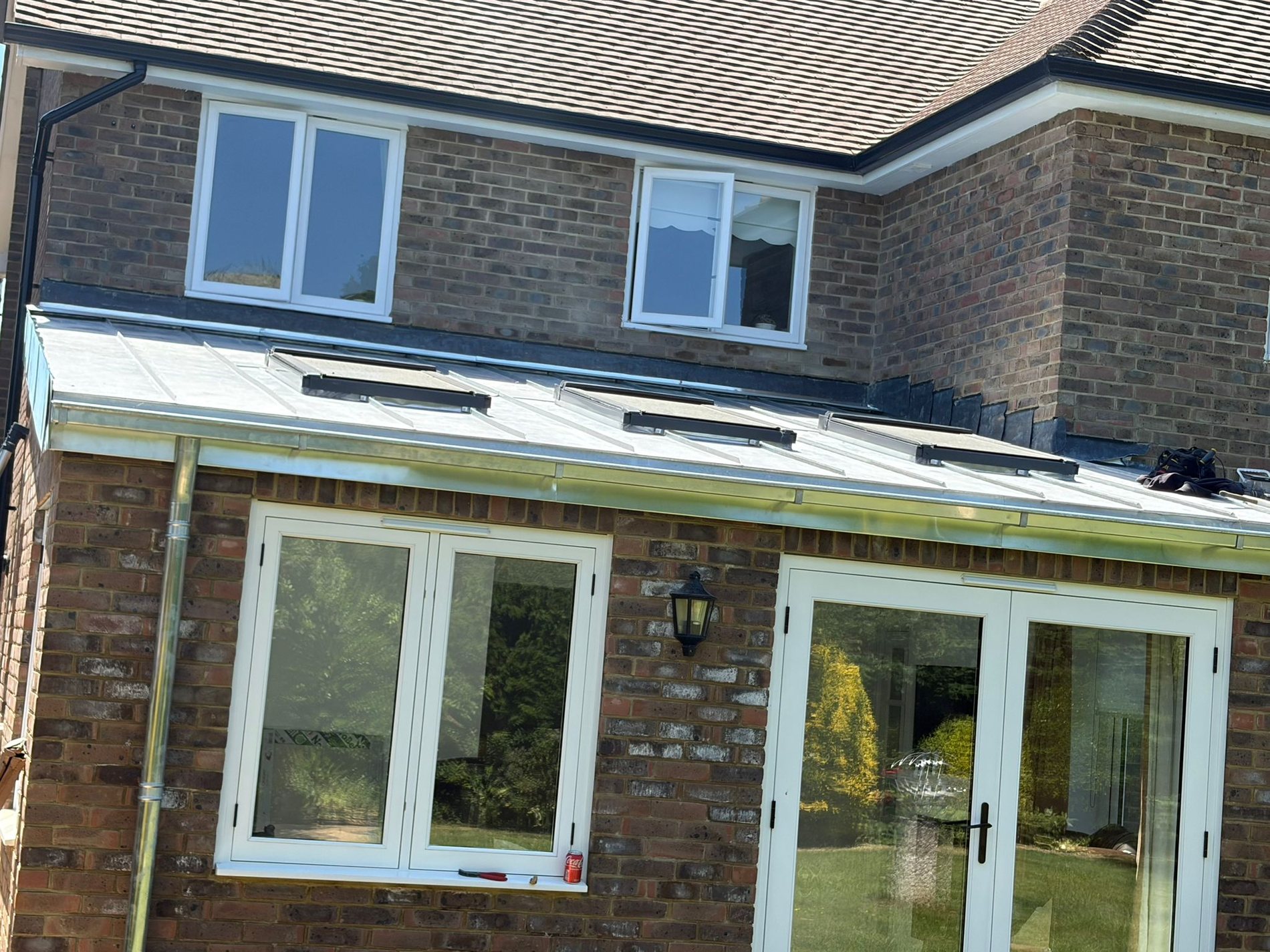 Natural zinc roof on a single storey rear extension, with rooflights and a gutter, meeting the brick wall of the house